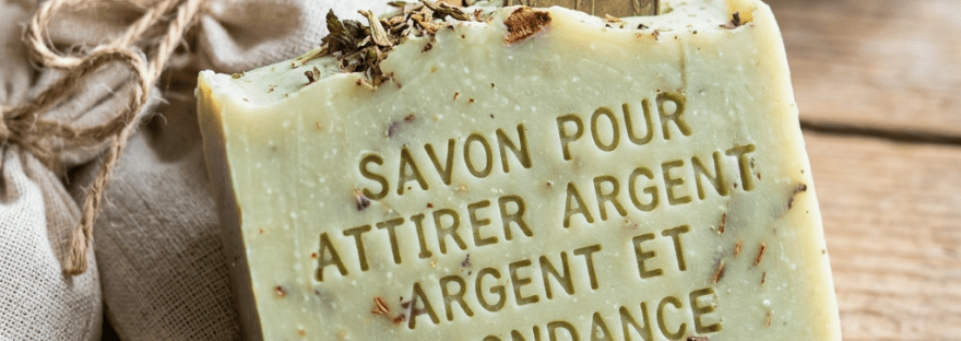 Herbal soap bar with French text about attracting money and a coin behind it